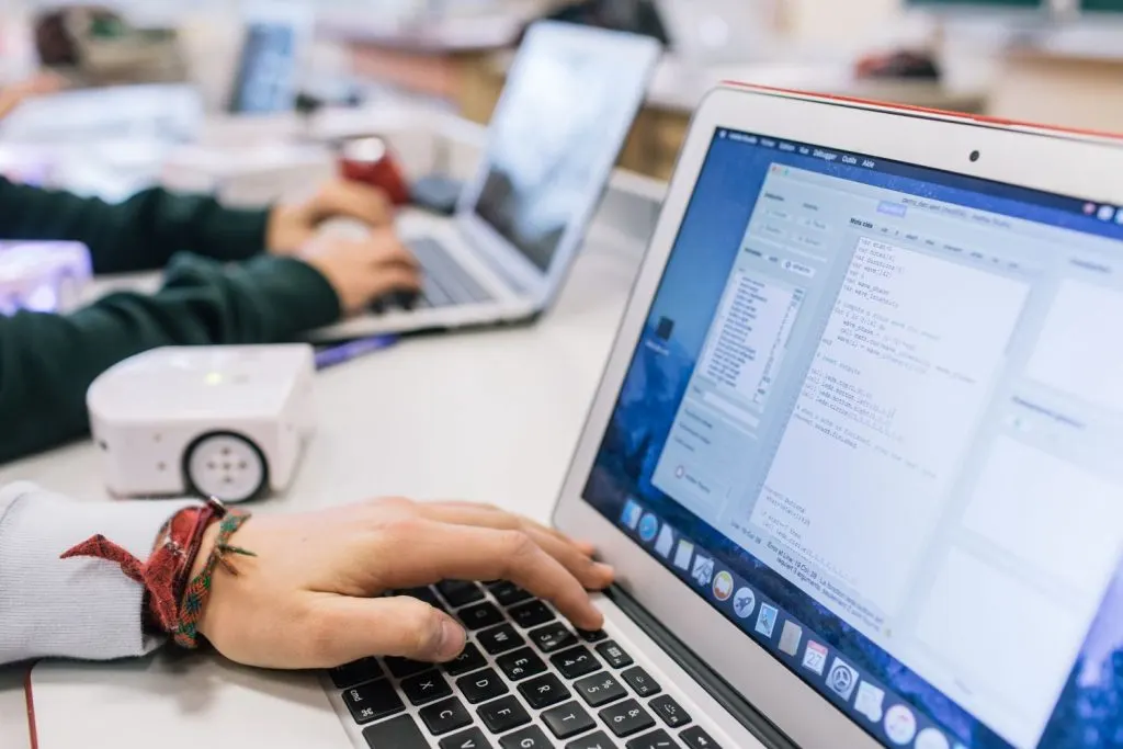 Élèves de l'institut Florimont programmant sur des ordinateurs portables, avec un petit robot éducatif sur la table